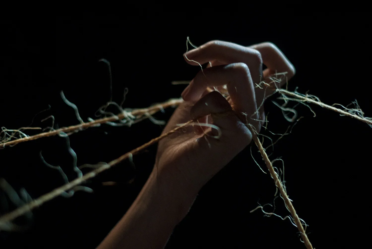 En hand håller i trådar mot en mörk bakgrund.