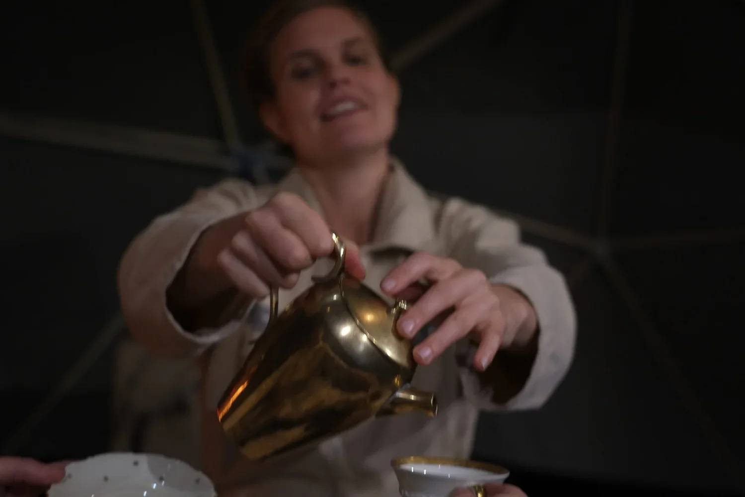 Kvinna häller te ur en guldfärgad tekanna i en kopp.