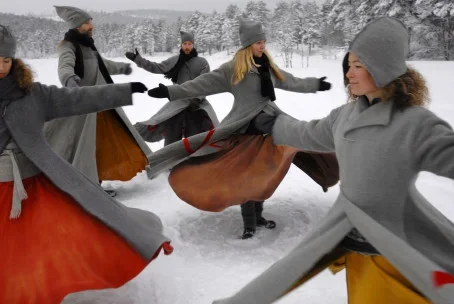 Flera personer som dansar i snön, klädda i vinterkläder, i en vinterlandskap.