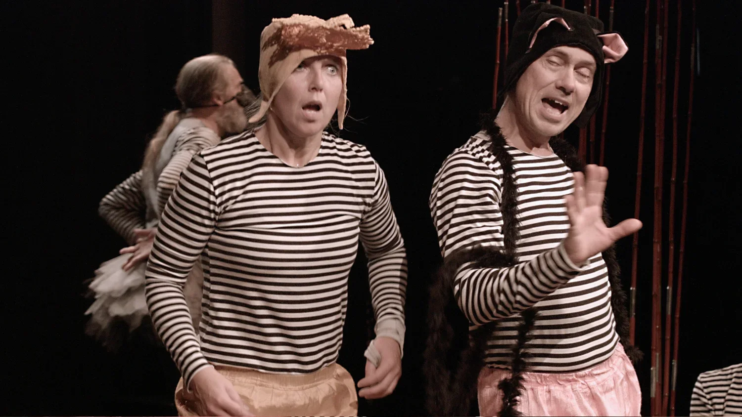 Två personer i svartvita randiga tröjor, båda med olika hattar, framträder i en scen.