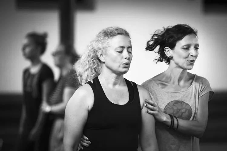 Två kvinnor som deltar i en workshop, med personer i bakgrunden.