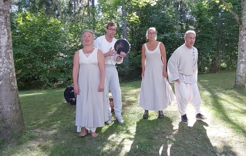 Fyra personer står på gräset i en skog, klädda i vita kläder.