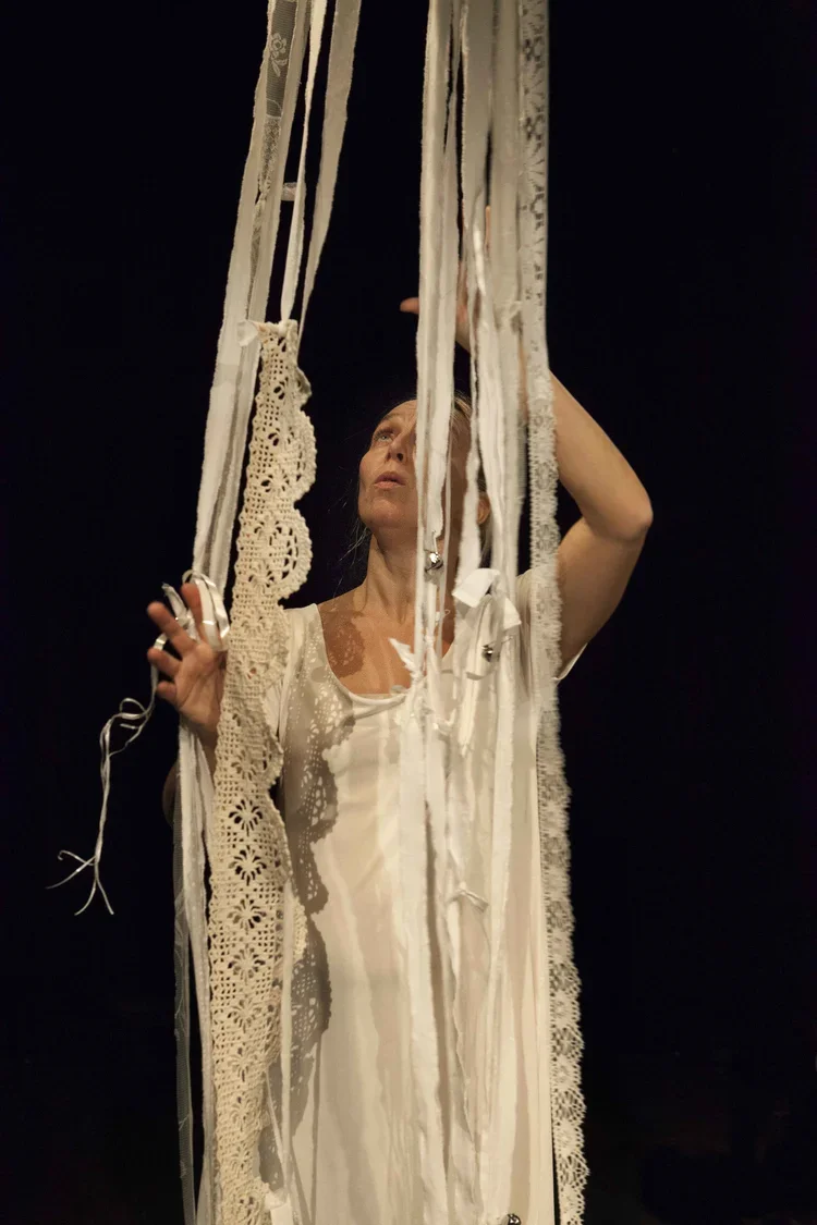 En kvinna står bakom en ram av trasor och tyger, som hänger ner framför henne.