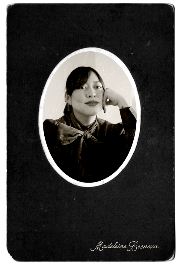 Retrato en blanco y negro de una mujer sonriendo, apoyando su rostro en su mano, enmarcada en un espejo ovalado. La foto está en una tarjeta negra con el nombre 'Madeleine Besneux' en la parte inferior.