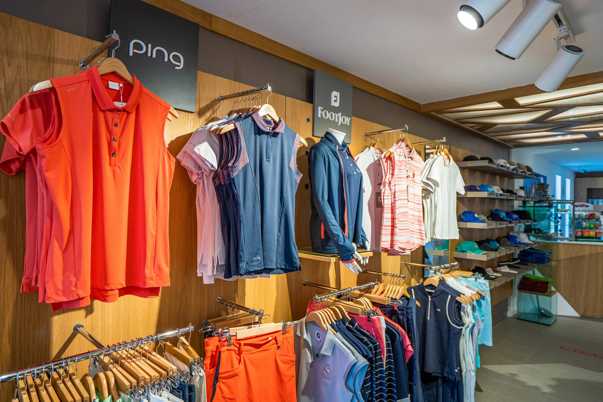 Ropa deportiva y accesorios en tienda, con marcas Ping y FootJoy en exhibición.