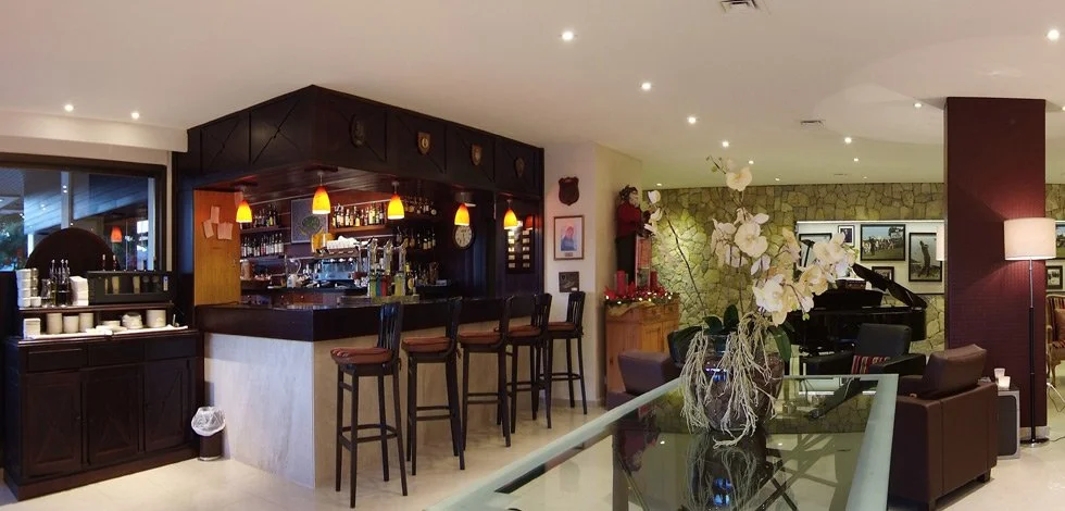 Bar con iluminación cálida, mesa de billar, piano, y decoración con plantas y cuadros en un ambiente acogedor.