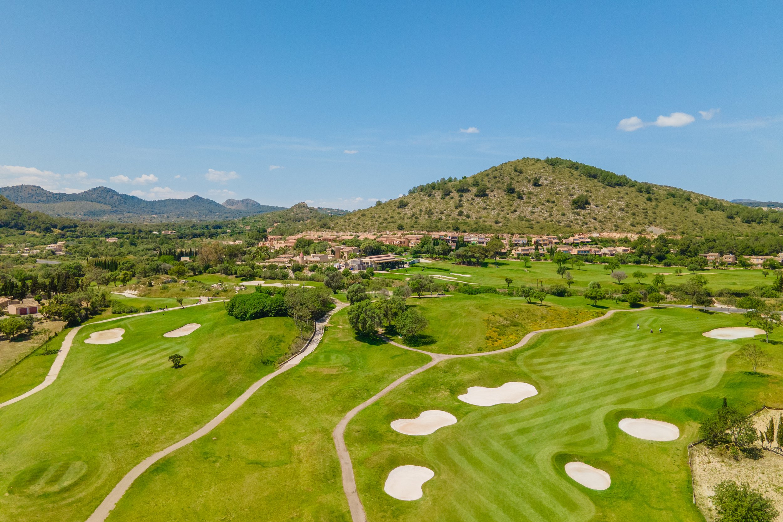 Campos de golf con búnker en primer plano y colinas verdes en el fondo, bajo un cielo despejado.