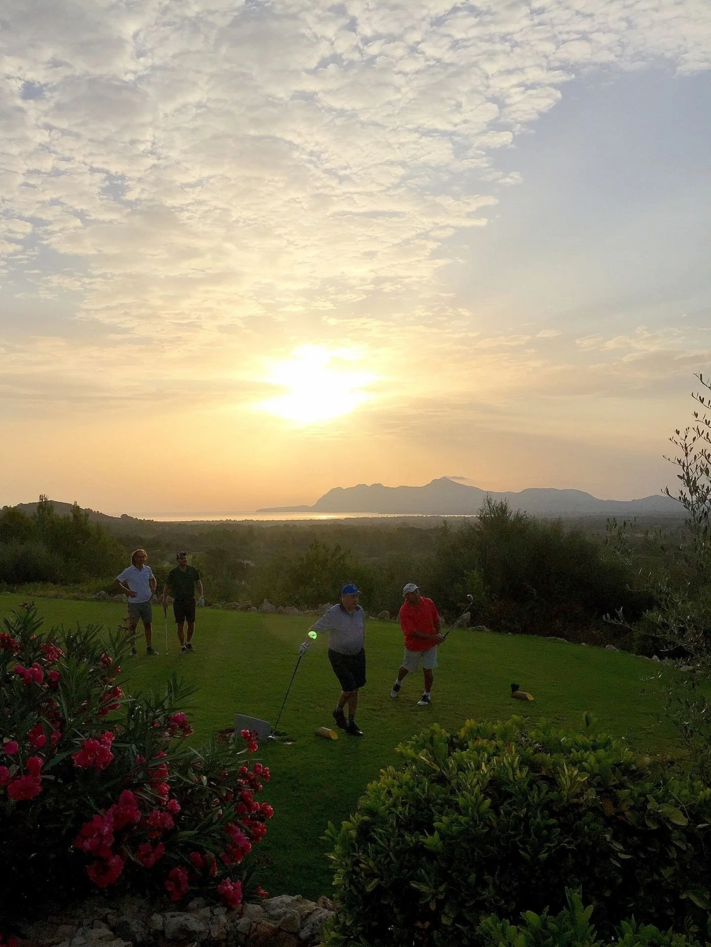 Cuatro personas jugando golf al atardecer en un campo rodeado de vegetación y con montañas a lo lejos.