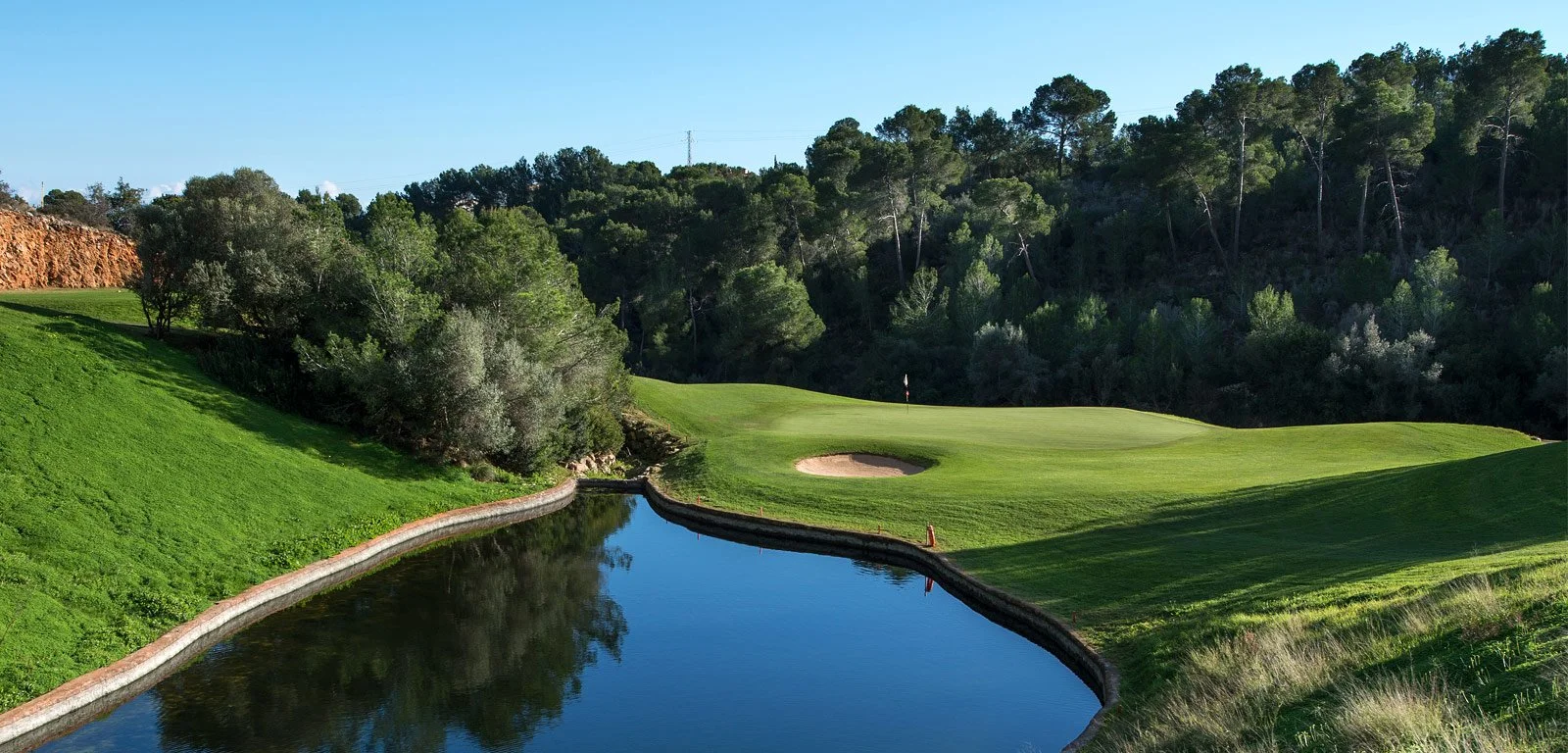Campo de golf con agua, arbustos, árboles y un hoyo con bandera