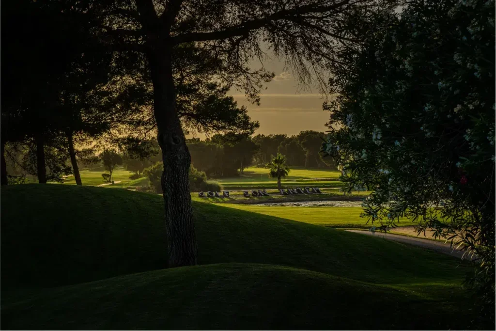 Un campo de golf al atardecer, árboles y un cartel que dice 'Course' y 'Pine'.