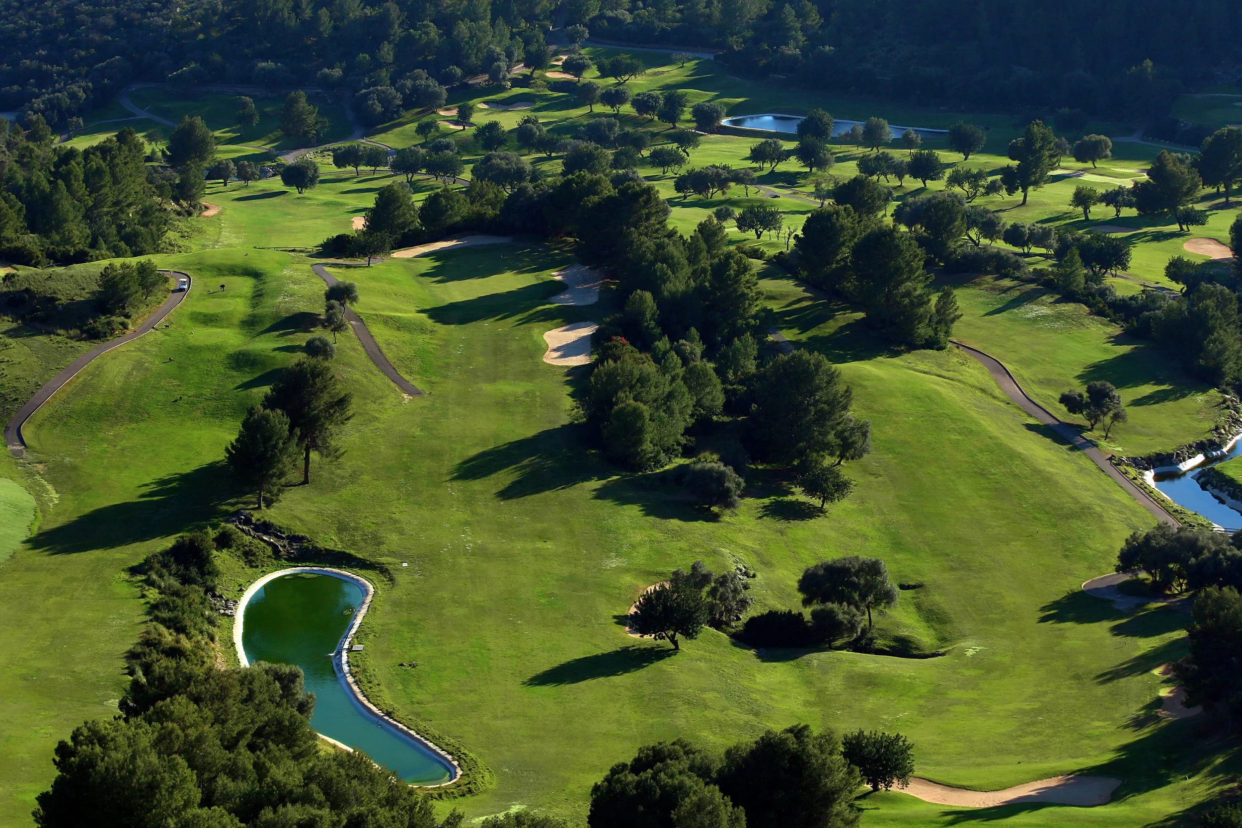 Vista aérea de un campo de golf rodeado de árboles verdes, con varios lagos y caminos pavimentados.