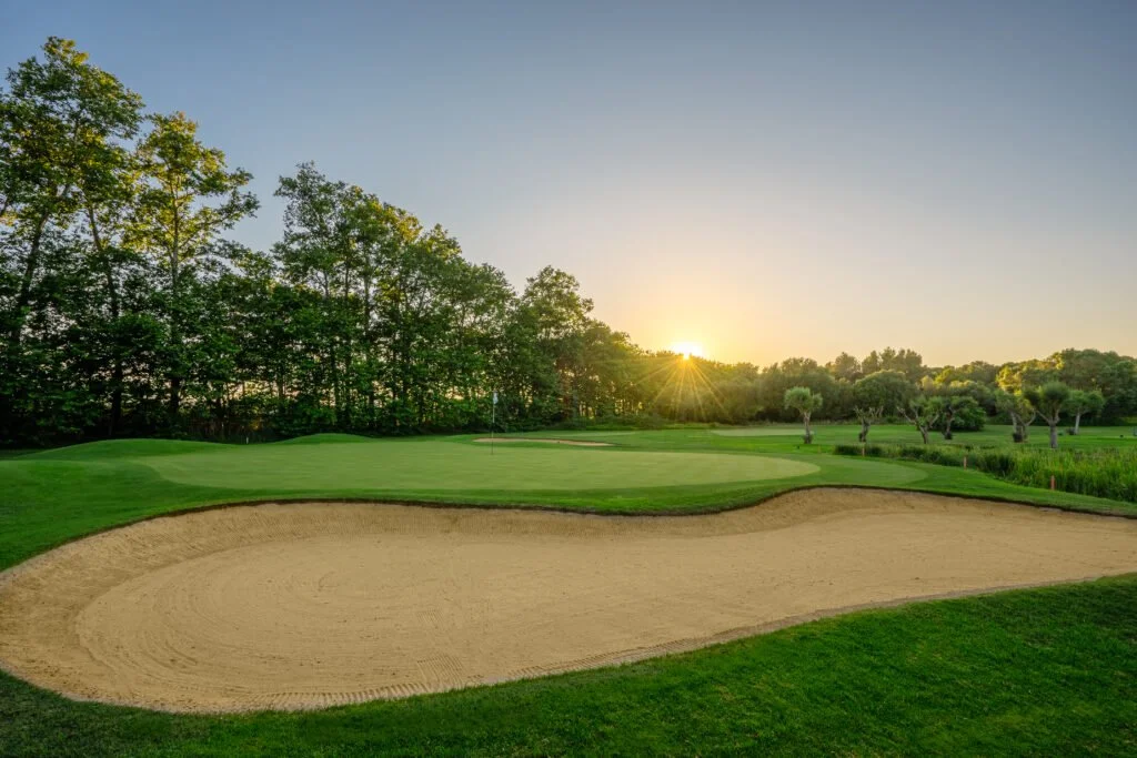 Campo de golf con zona de arena, grass, árboles y puesta de sol