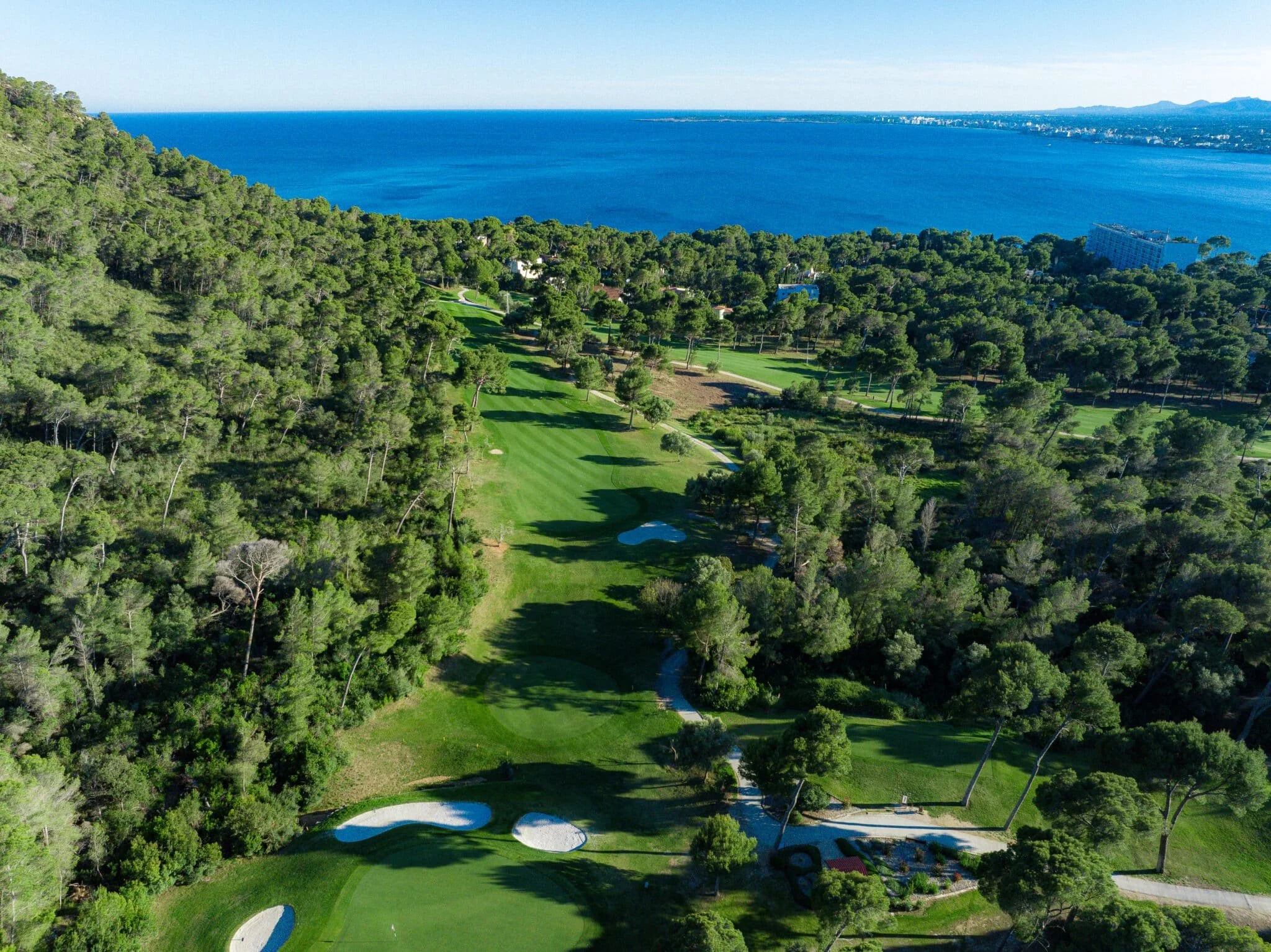 Vista aérea de un campo de golf rodeado de árboles y con el mar de fondo.