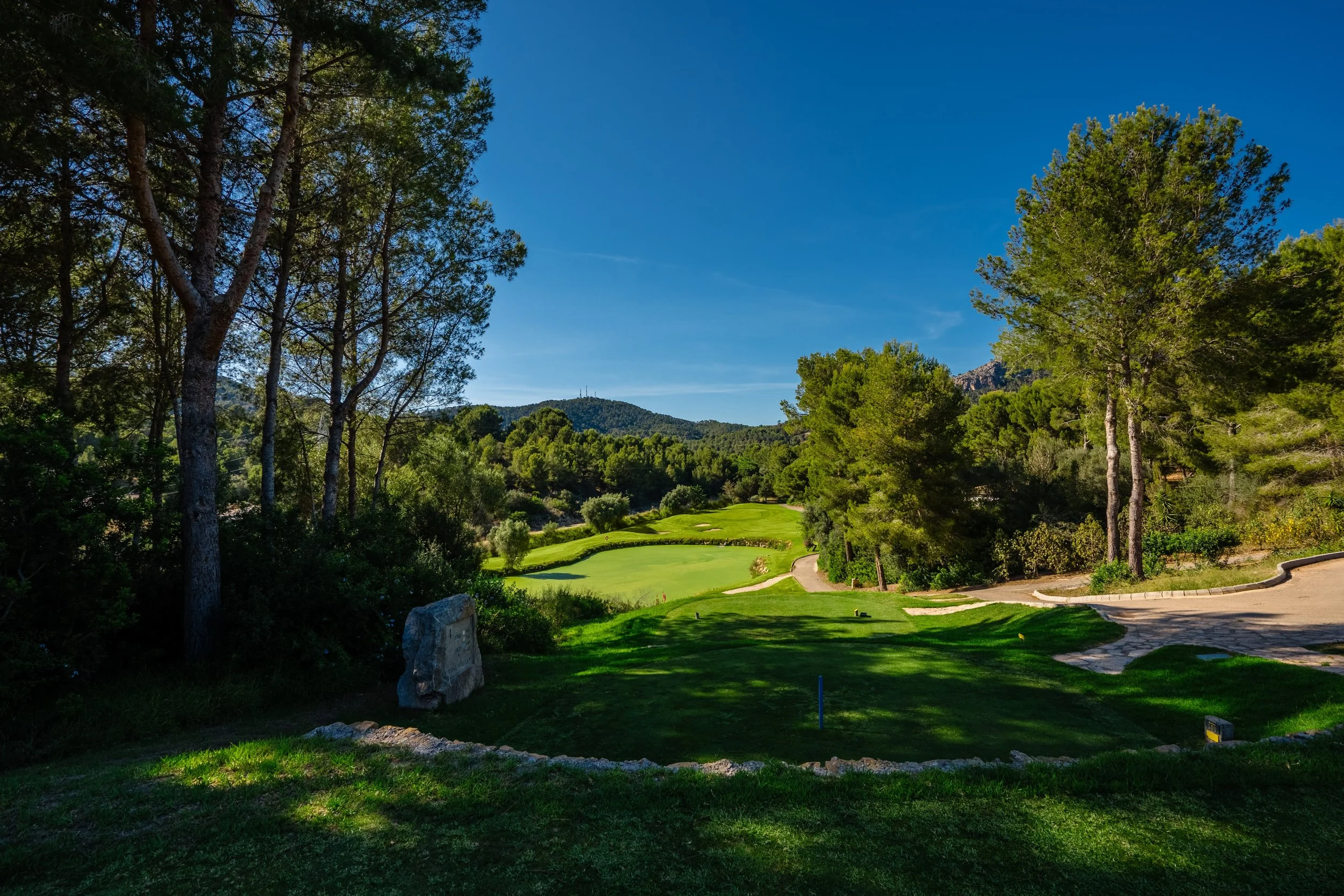 Cancha de golf rodeada de árboles y montañas bajo un cielo despejado.