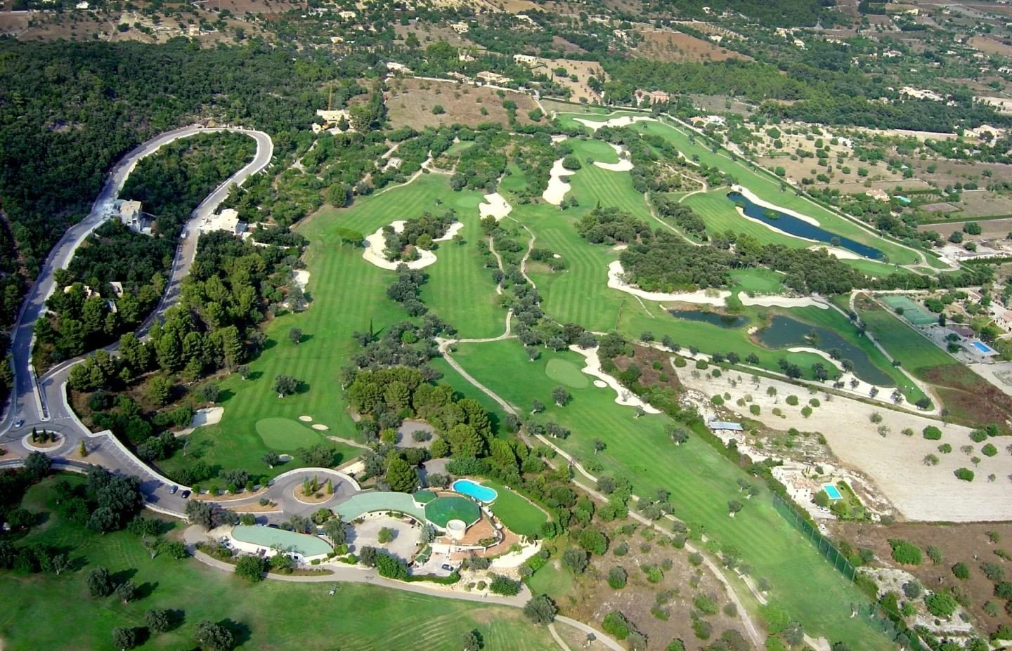 Vista aérea de un campo de golf con varios hoyos, árboles dispersos y lagos en el paisaje.