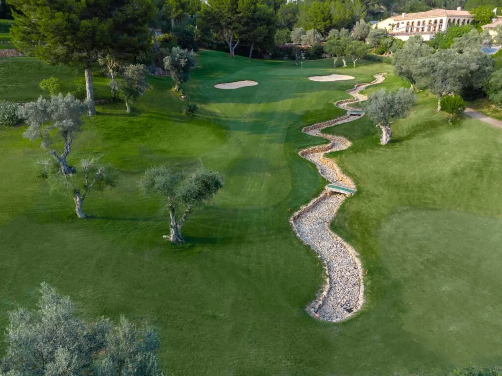 Vista aérea de un campo de golf con césped verde, árboles y un sendero de piedras en forma de zigzag.