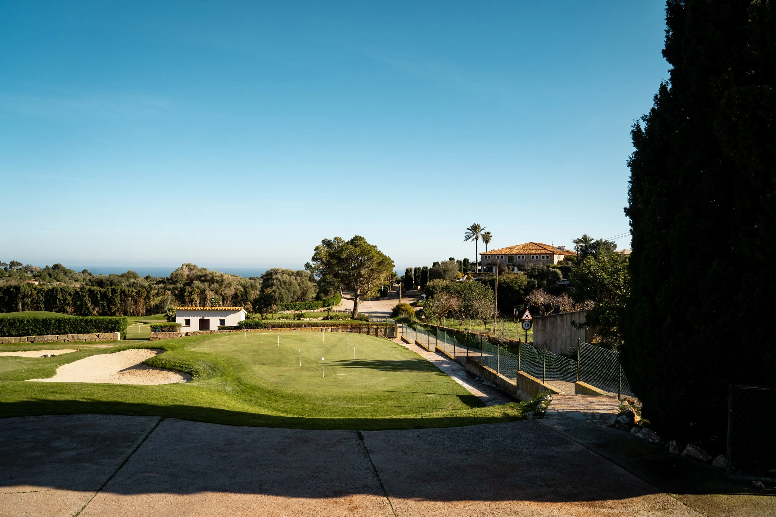 Campo de golf bajo un cielo despejado, con árboles y casas en el fondo.