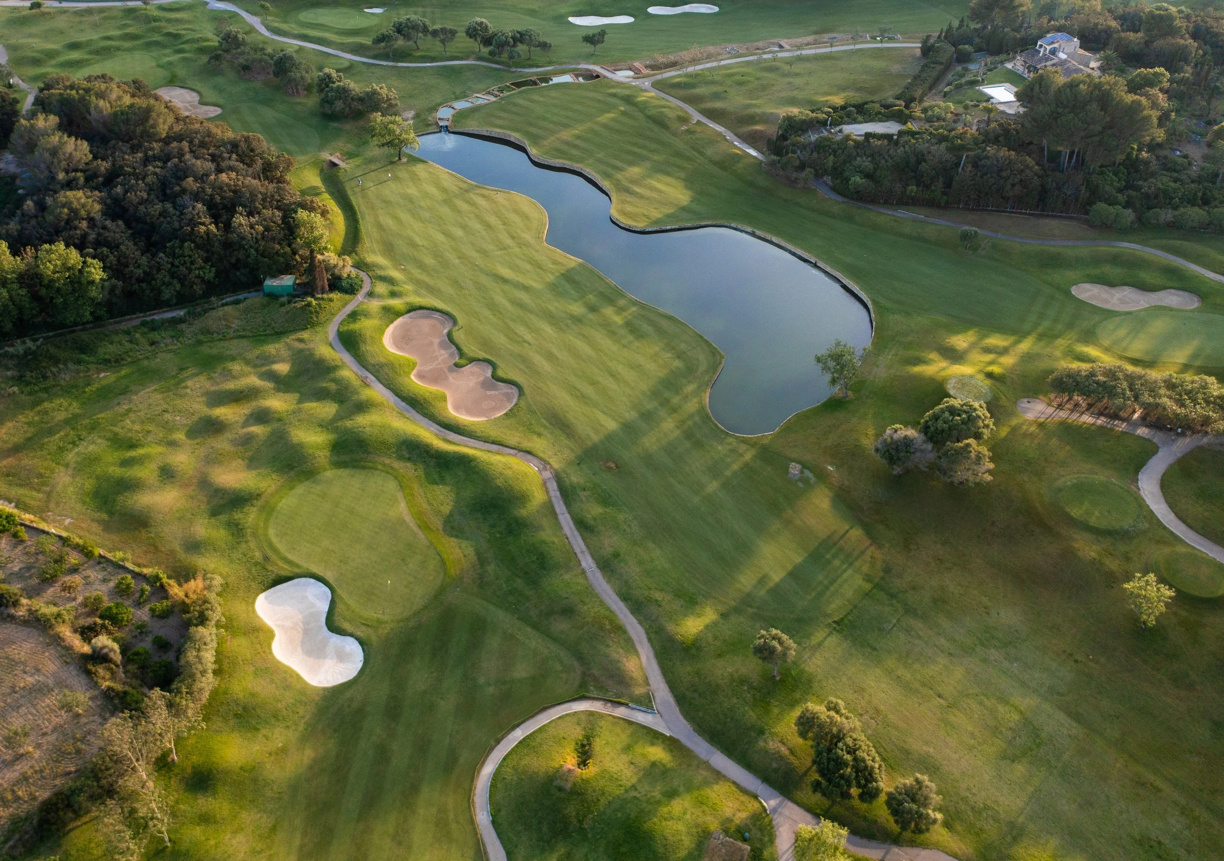 Vista aérea de un campo de golf con varios hoyos, arena y lagunas, rodeado de árboles y caminos.