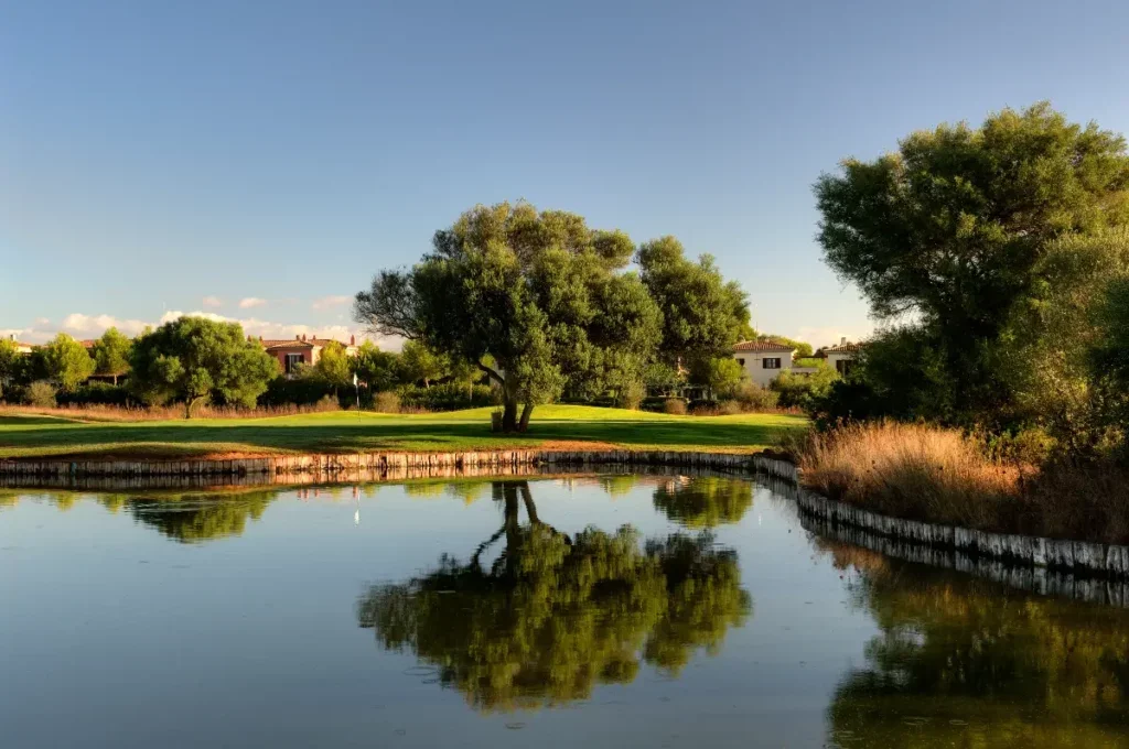Paisaje de un campo de golf con árboles y un lago que refleja el cielo y los árboles.
