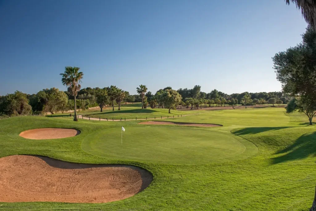Un campo de golf con césped bien cuidado, varios bunkers y árboles, en un día soleado y despejado.