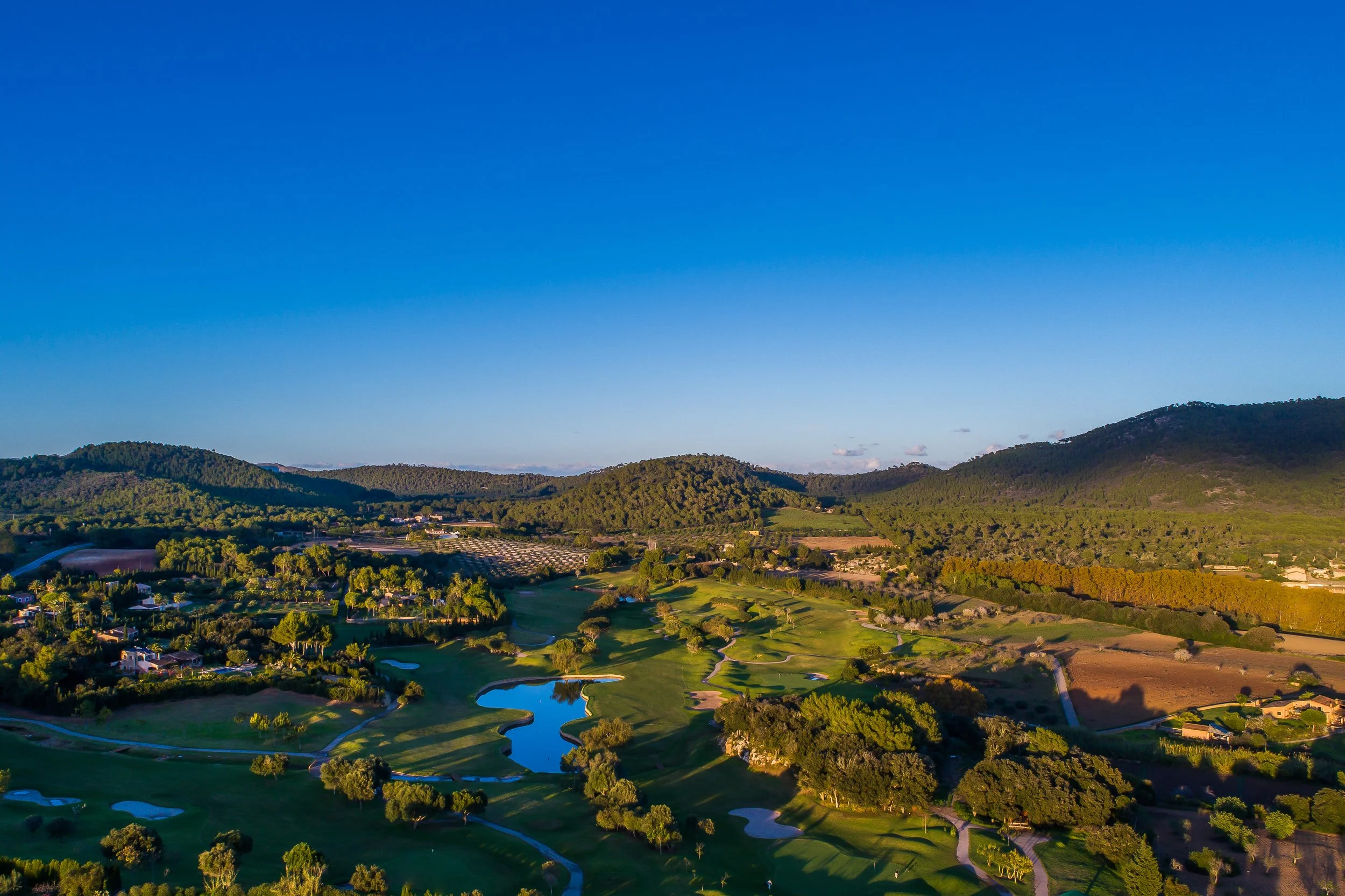 Vista aérea de un campo de golf rodeado de árboles y colinas con cielo despejado.