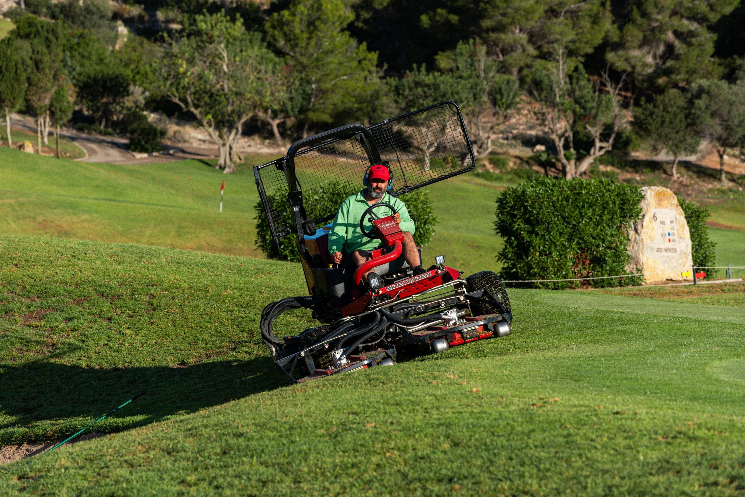 Hombre operando una máquina cortadora de césped en un campo de golf.