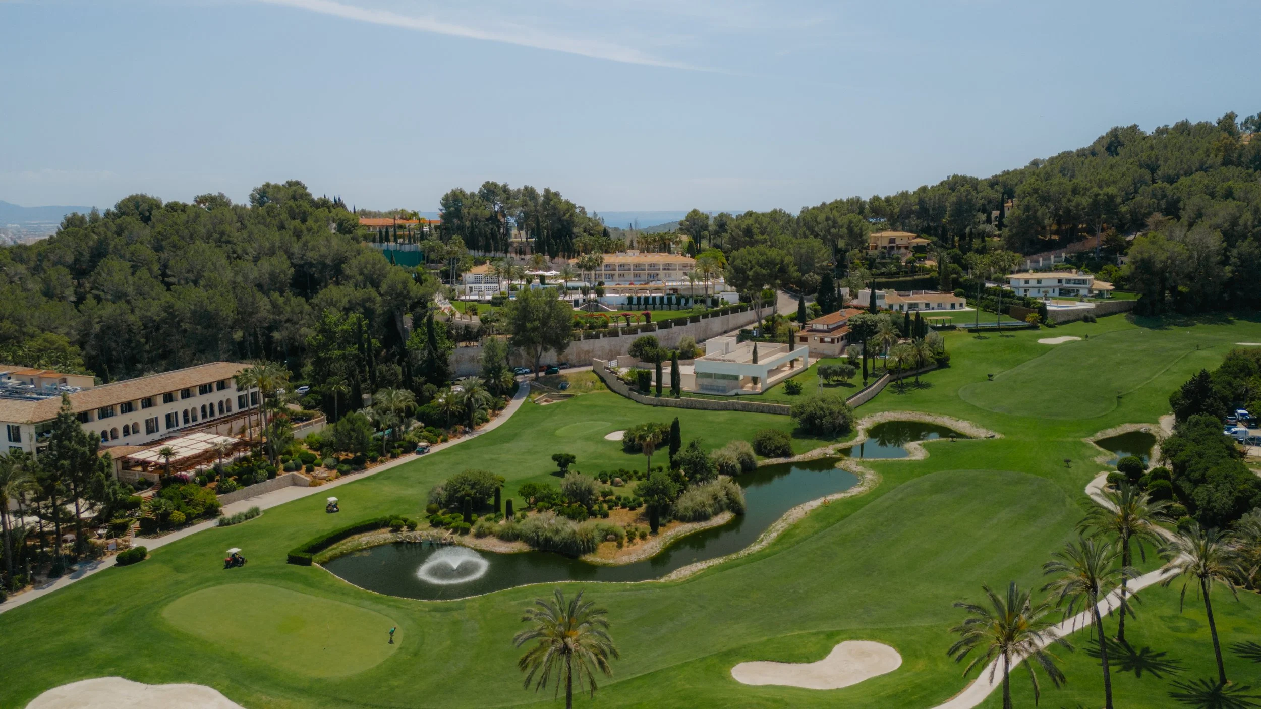 Campo de golf con lagunas, árboles y edificios residenciales en colinas.