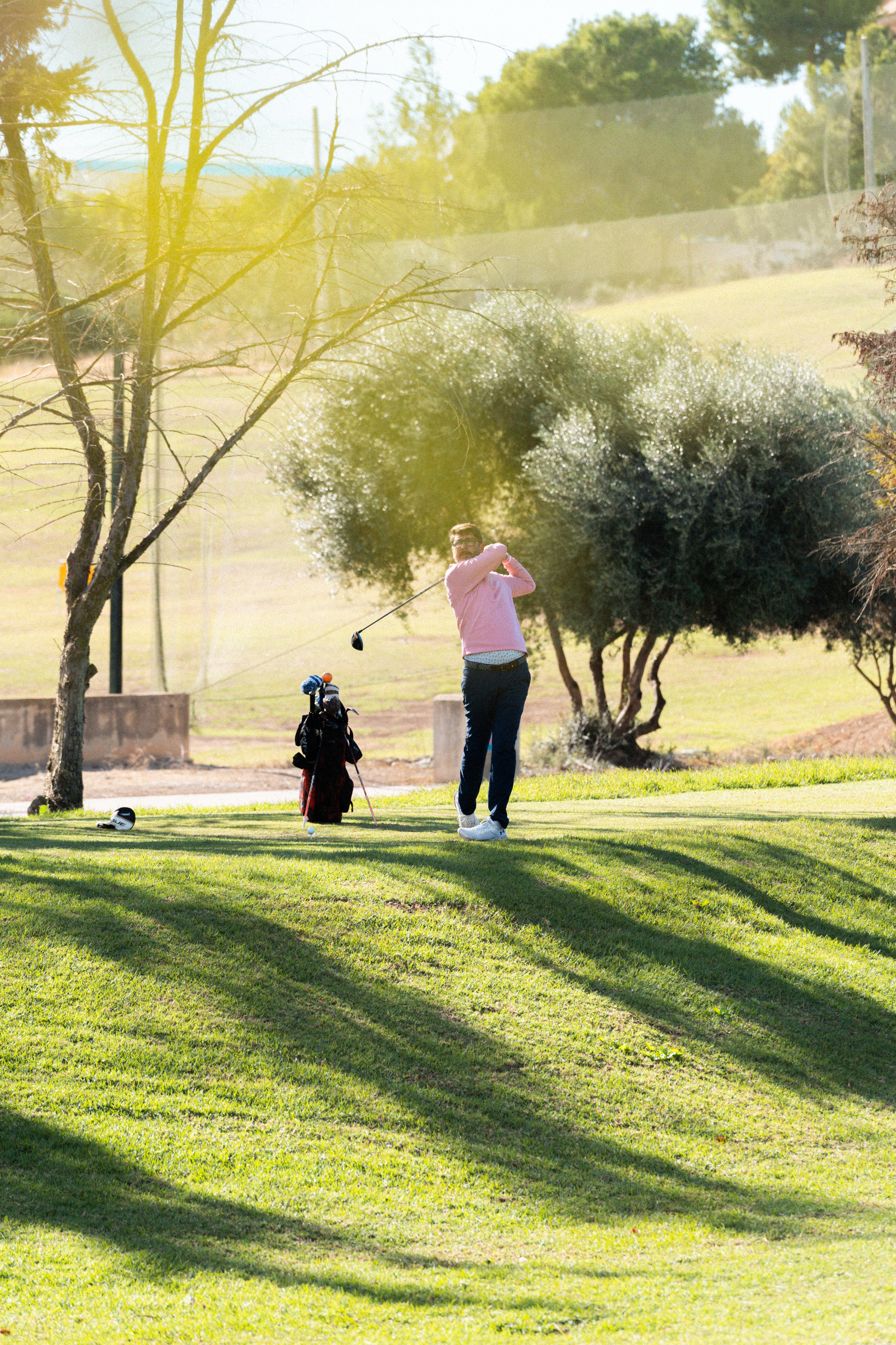 Mujer jugando al golf en un campo con árboles y sombra enrejada al fondo