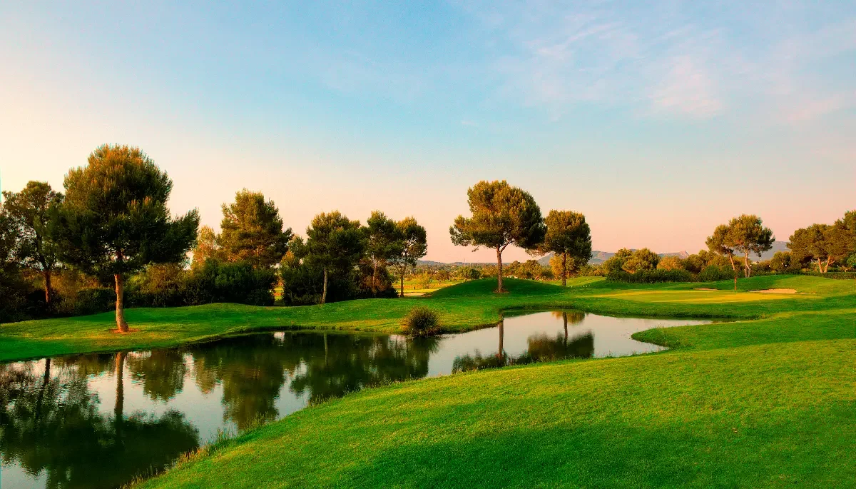 Un campo de golf con árboles y un pequeño lago reflejando el cielo y la vegetación.