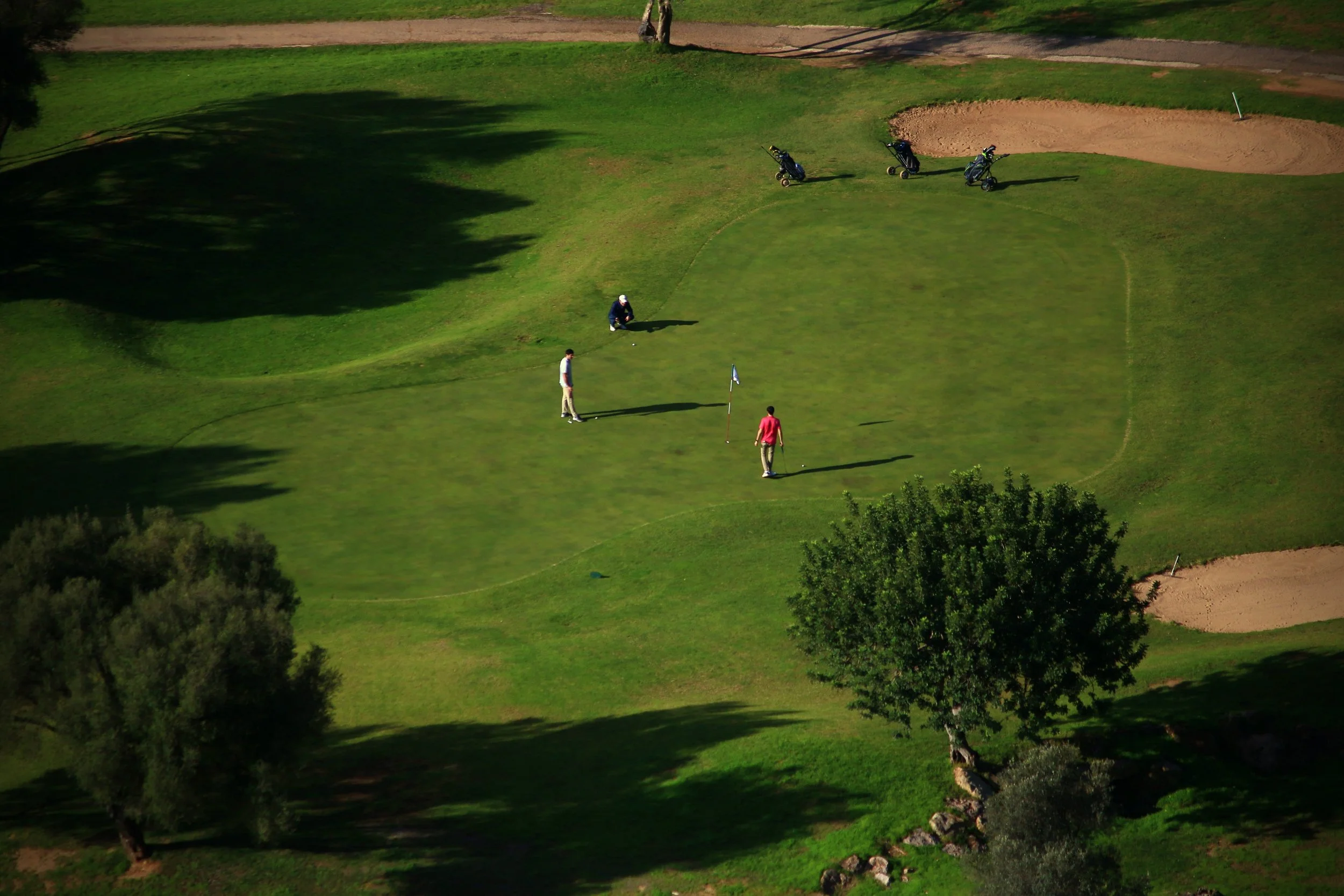 Jugadores de golf en un campo alineando para hacer un tiro. Hay botes con palos de golf y un foro en el campo.