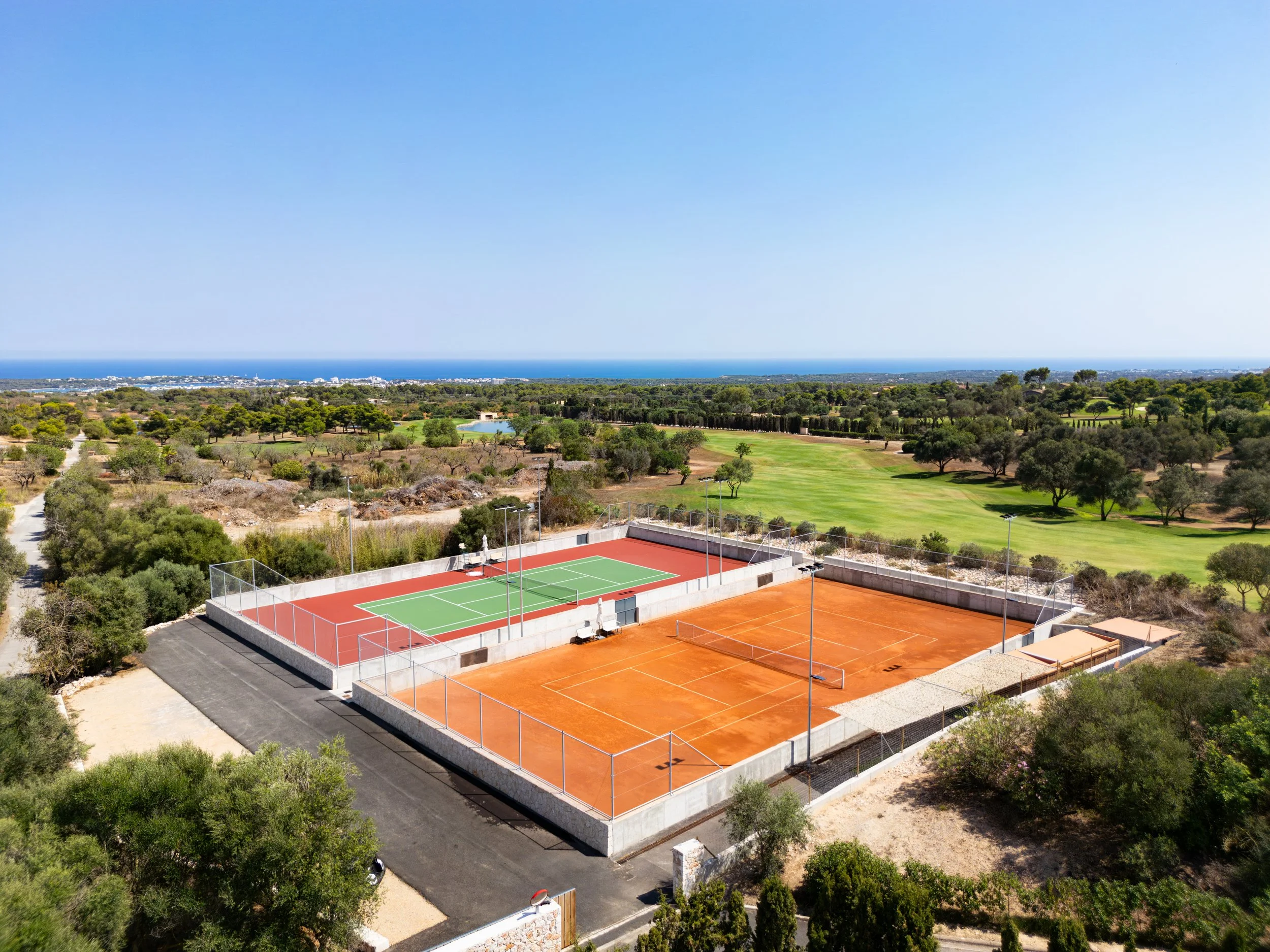 Cancha de tenis y pádel con paisaje de áreas verdes y árboles, vista al mar en la distancia, cielo despejado, en una zona de campo.