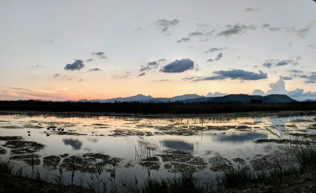 Paisaje natural con lago, montañas al fondo y cielo con nubes al atardecer.