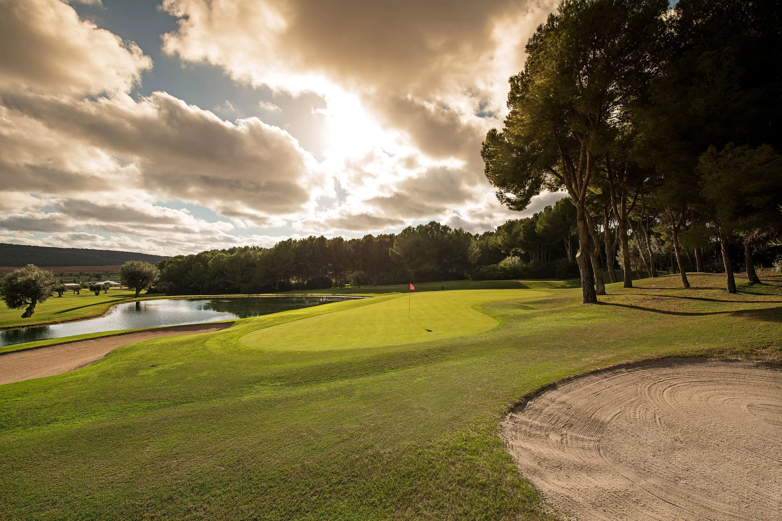 Campo de golf con agua, árboles y un sendero, bajo un cielo con nubes.