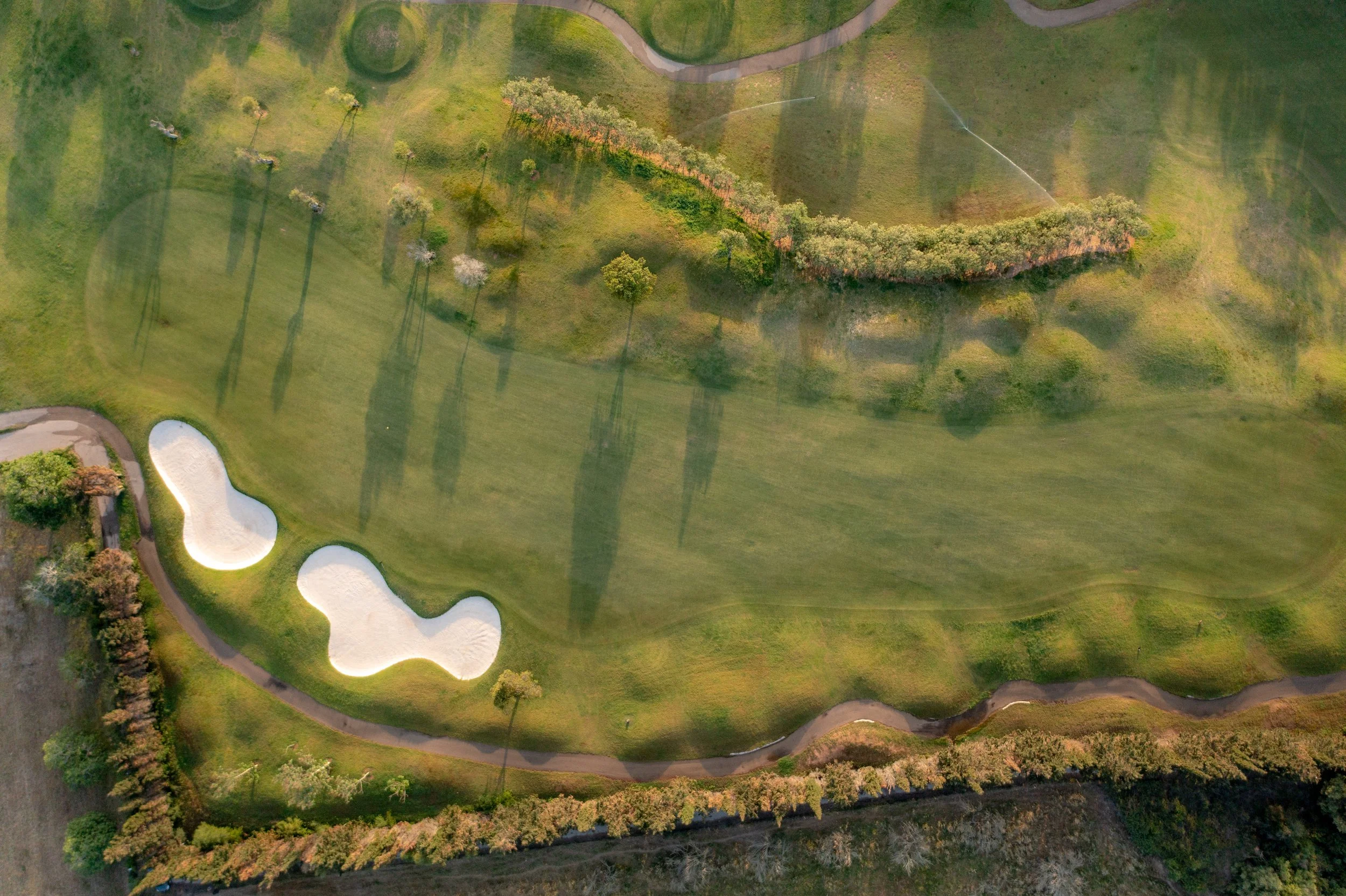 Vista aérea de un campo de golf con dos obstáculos de arena y caminos pavimentados rodeados de árboles y césped bien cuidado.