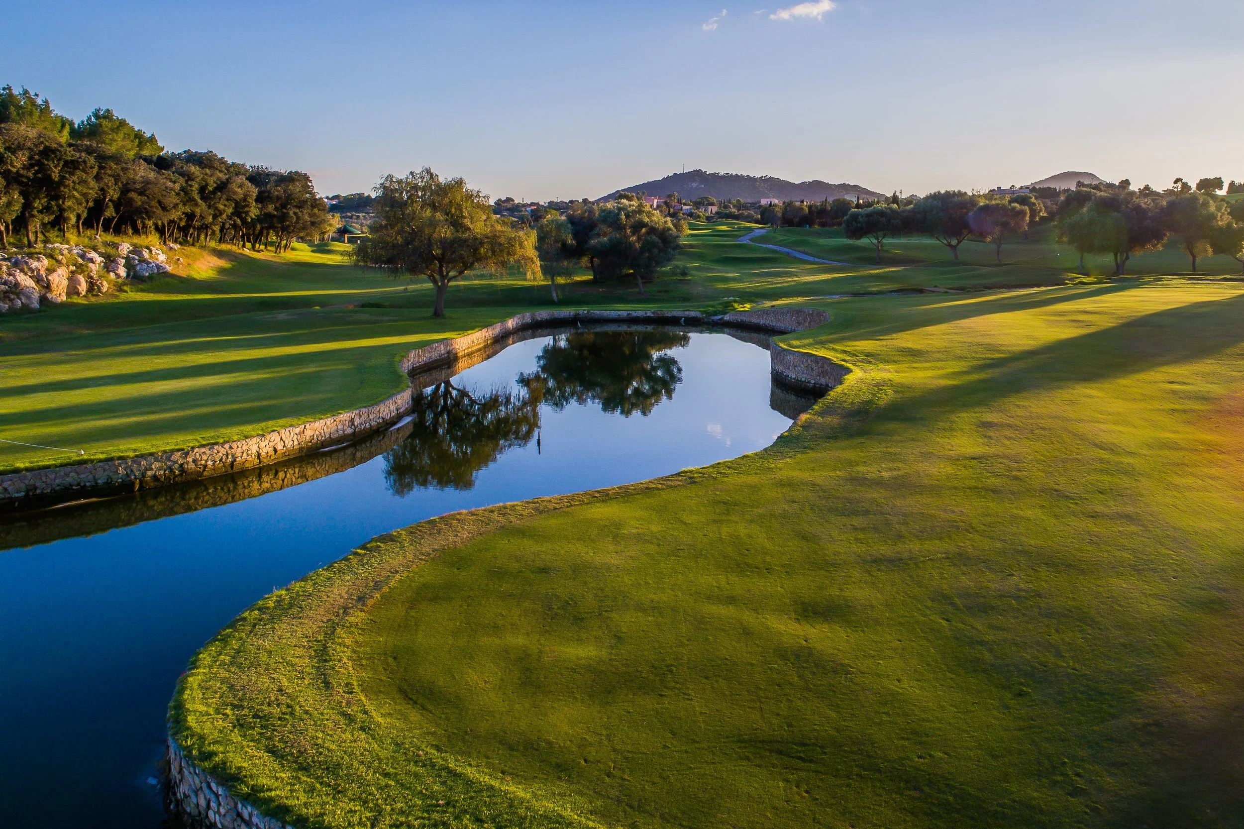 Campo de golf con agua y árboles al atardecer