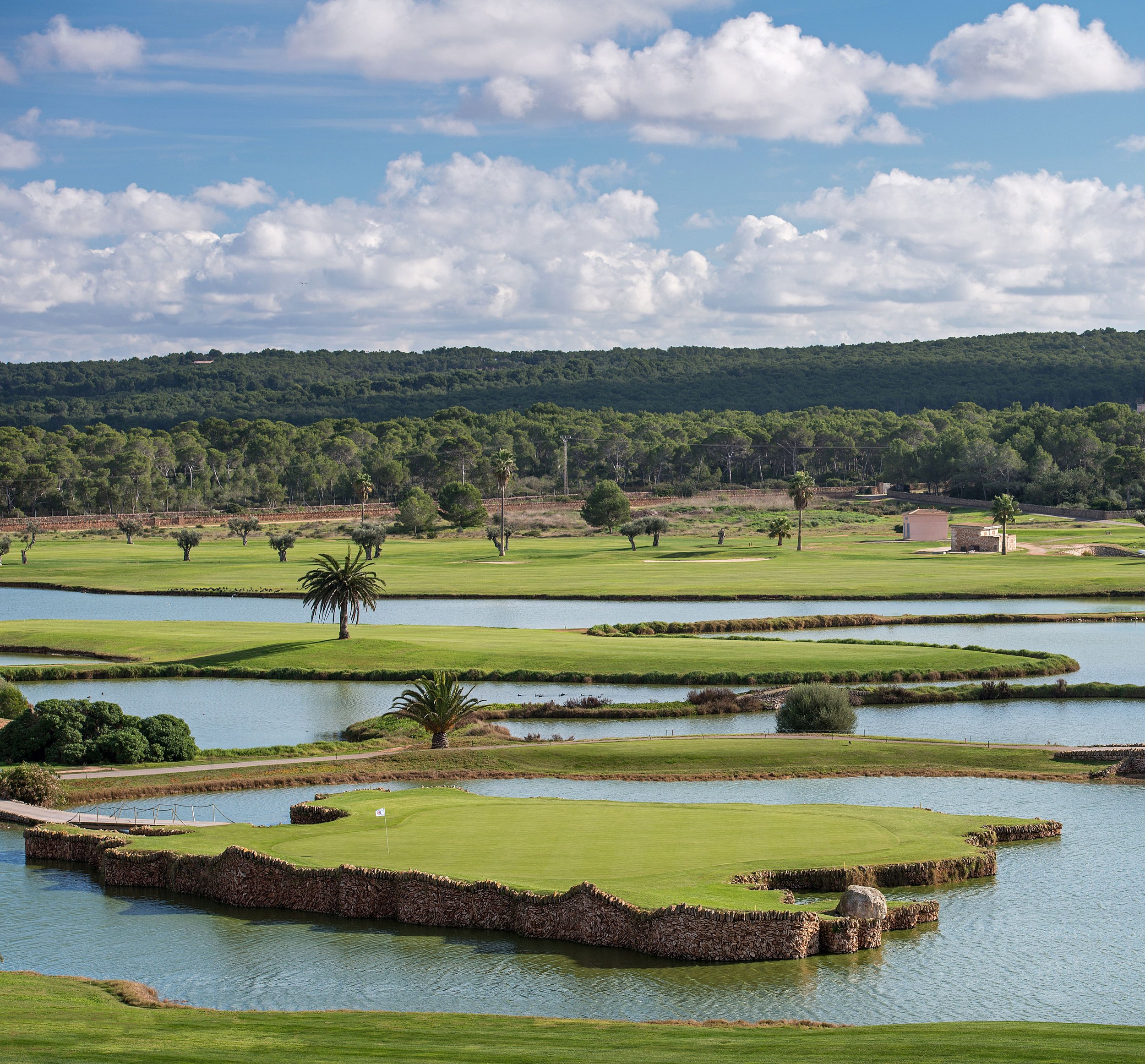Campo de golf con lagunas, árboles y colinas bajo un cielo con nubes