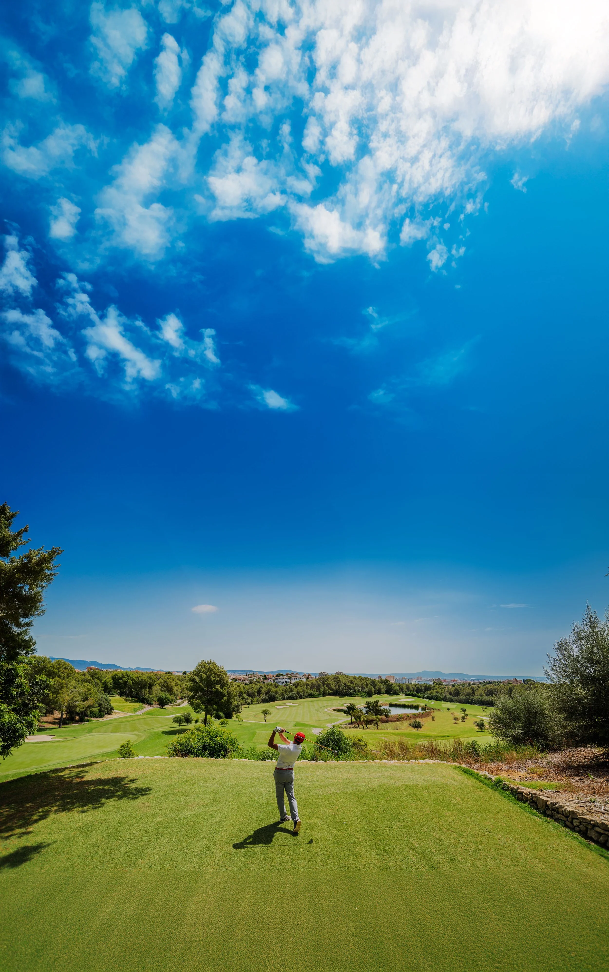 Jugador de golf en un campo con cielo despejado y nublado, rodeado de árboles y vegetación.