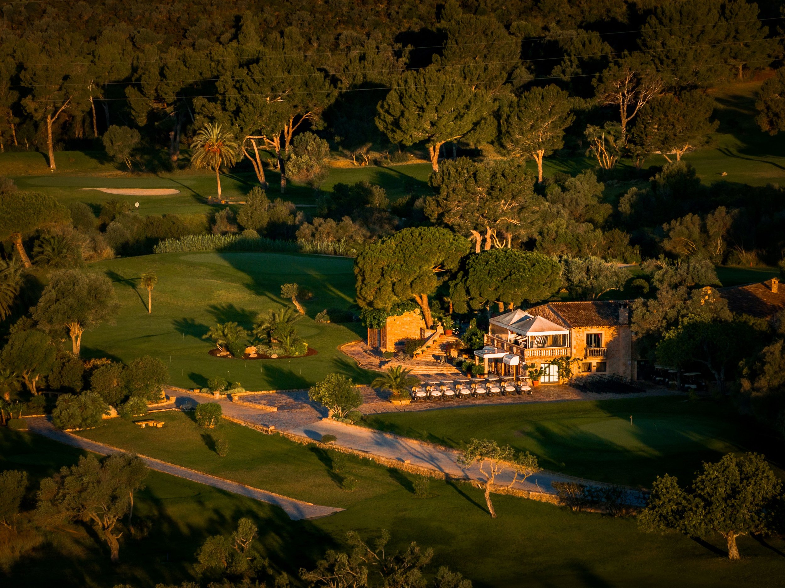 Atardecer sobre un campo de golf rodeado de árboles y casas con castañas, con sombras largas y cálidos tonos dorados.