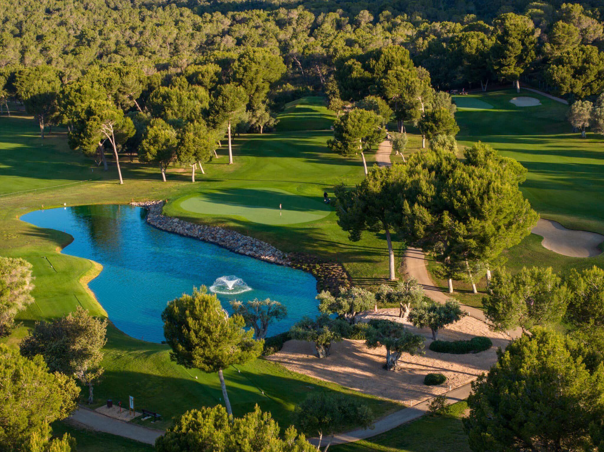 Campo de golf con estanque y árboles, con caminos y áreas de arena en un entorno natural.