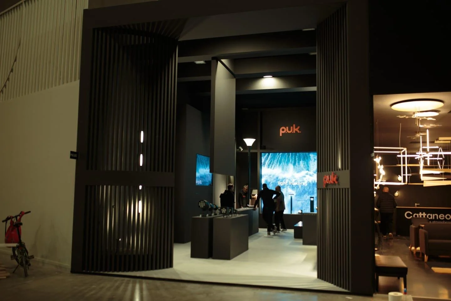 Interno di un negozio o esposizione di prodotti tecnologici con varie persone, schermi e luci moderne.