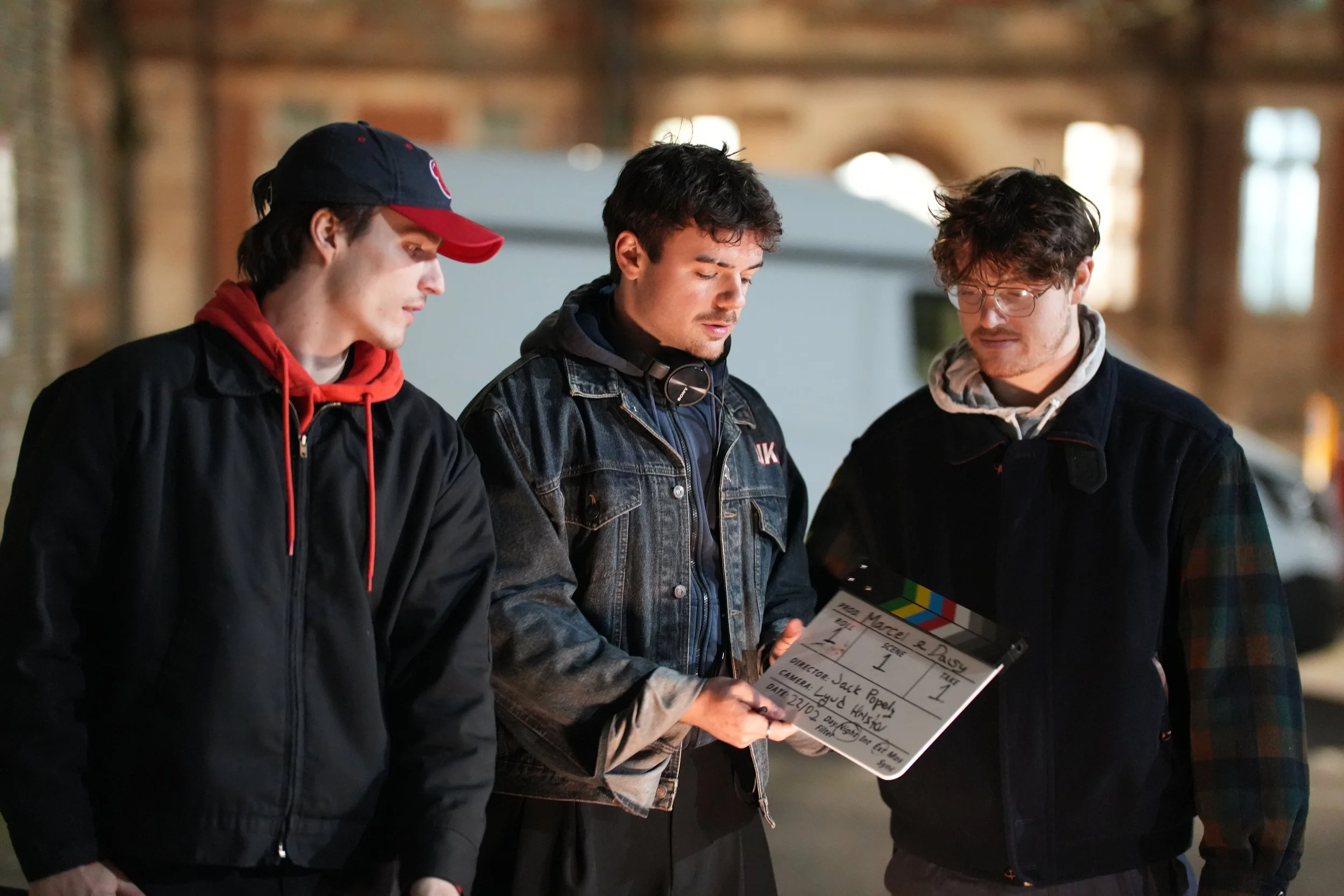 Three men standing together on a film set, reviewing a clapperboard.