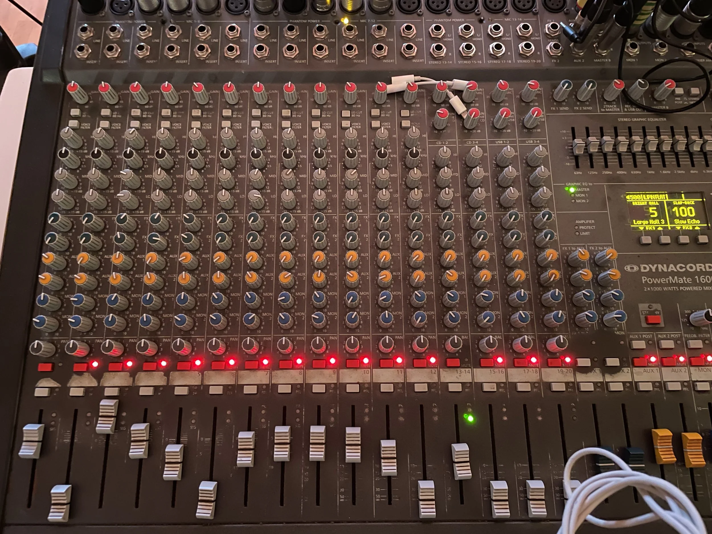 An audio mixing console with numerous knobs, sliders, and buttons used for sound control, with a digital display and cable connections.
