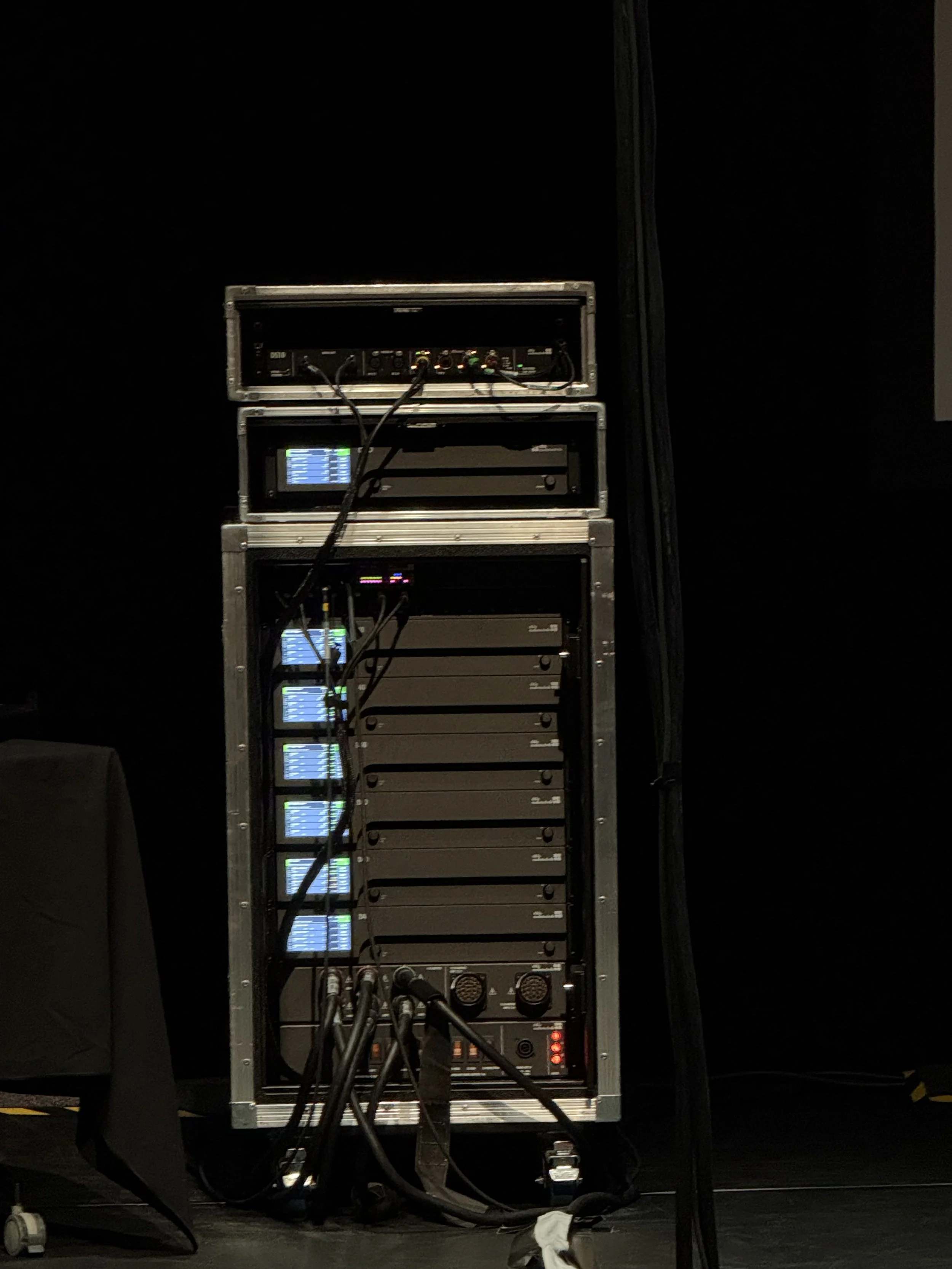 A rack of audio equipment with multiple devices connected by cables, set against a black background.