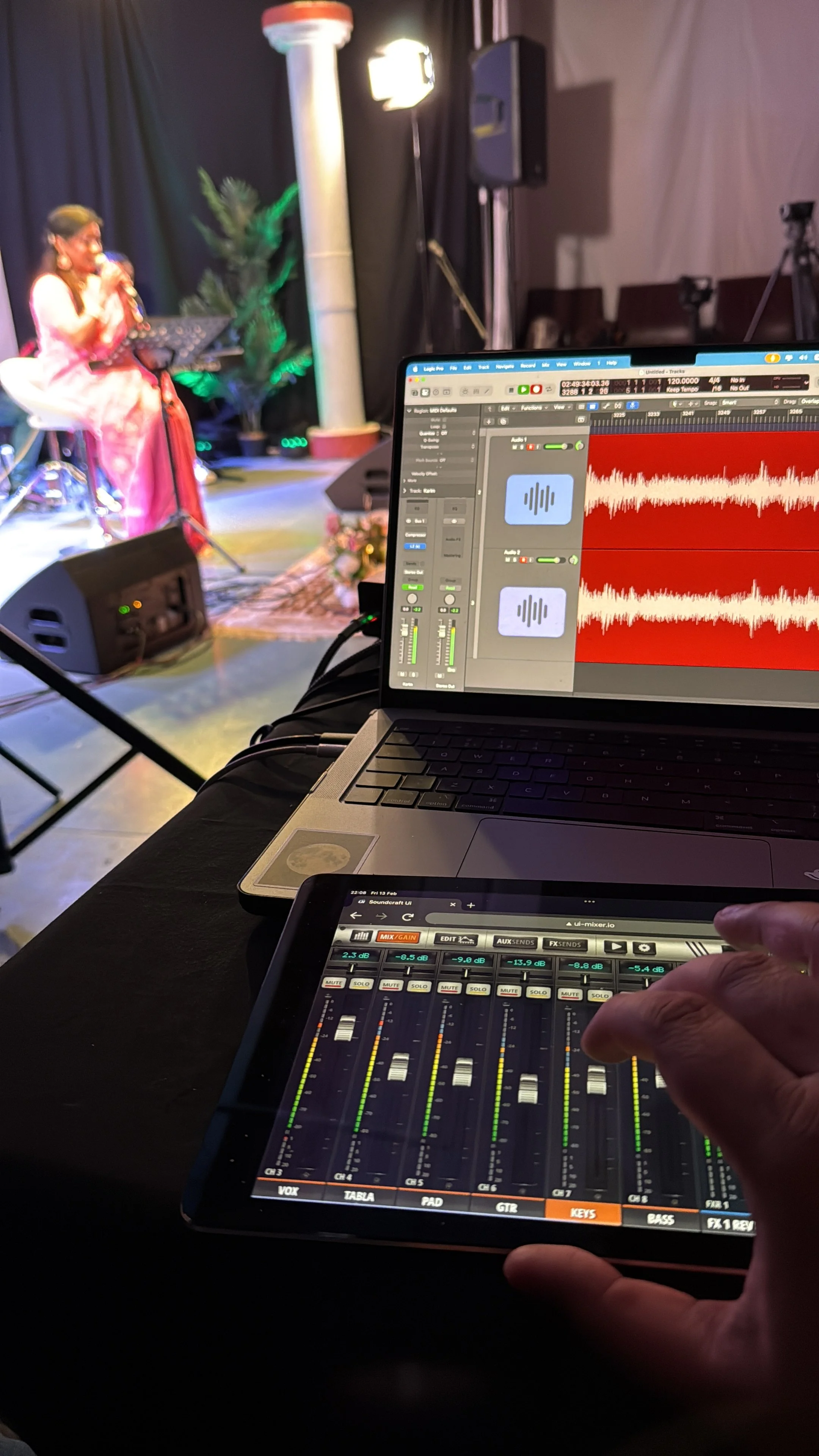 Close-up of audio mixing equipment displaying sound levels, with performer on stage in the background singing into a microphone.