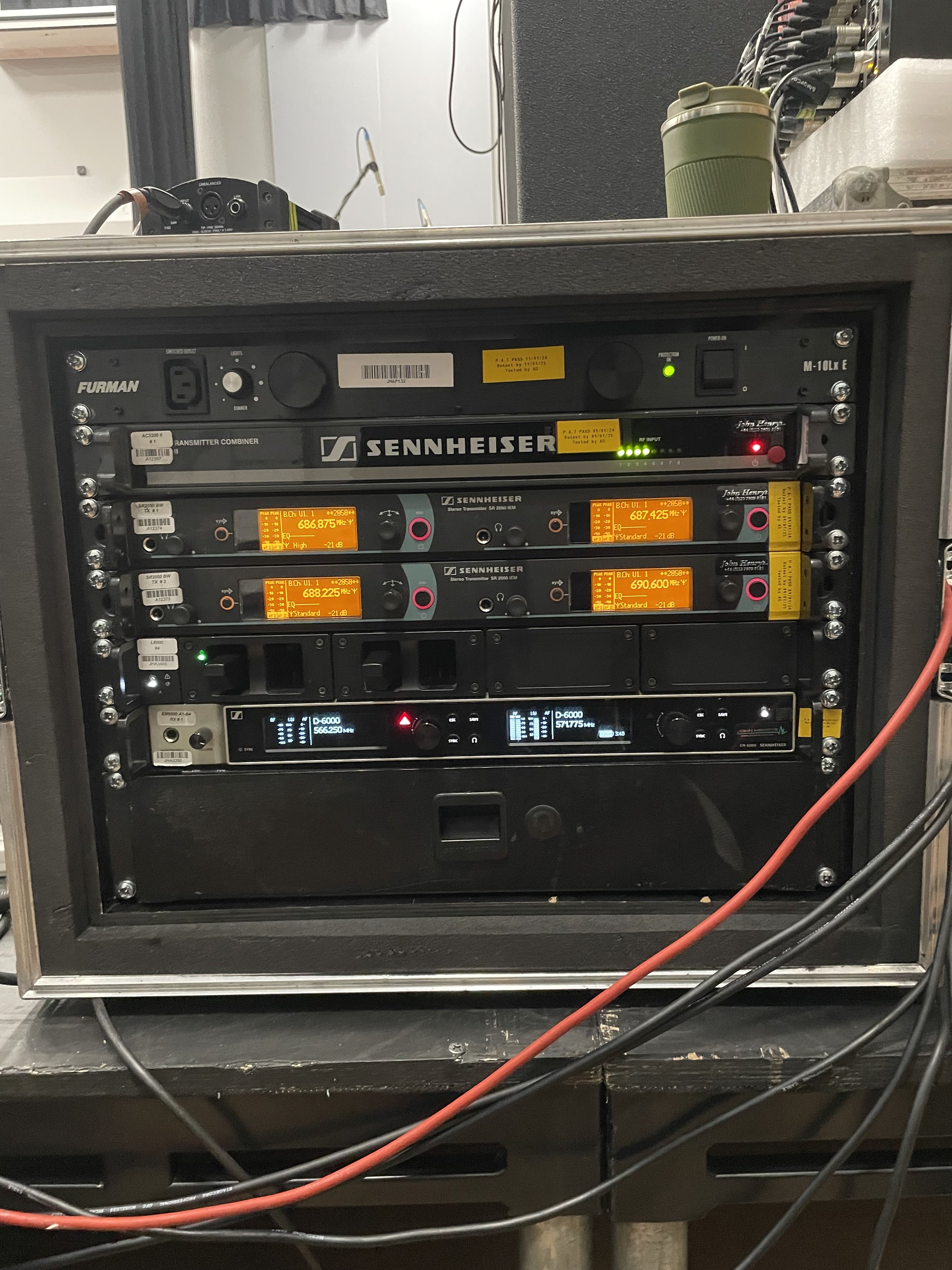 A rack of audio equipment including a Sennheiser transmitter, receiver, and other audio components, with multiple cables connected.