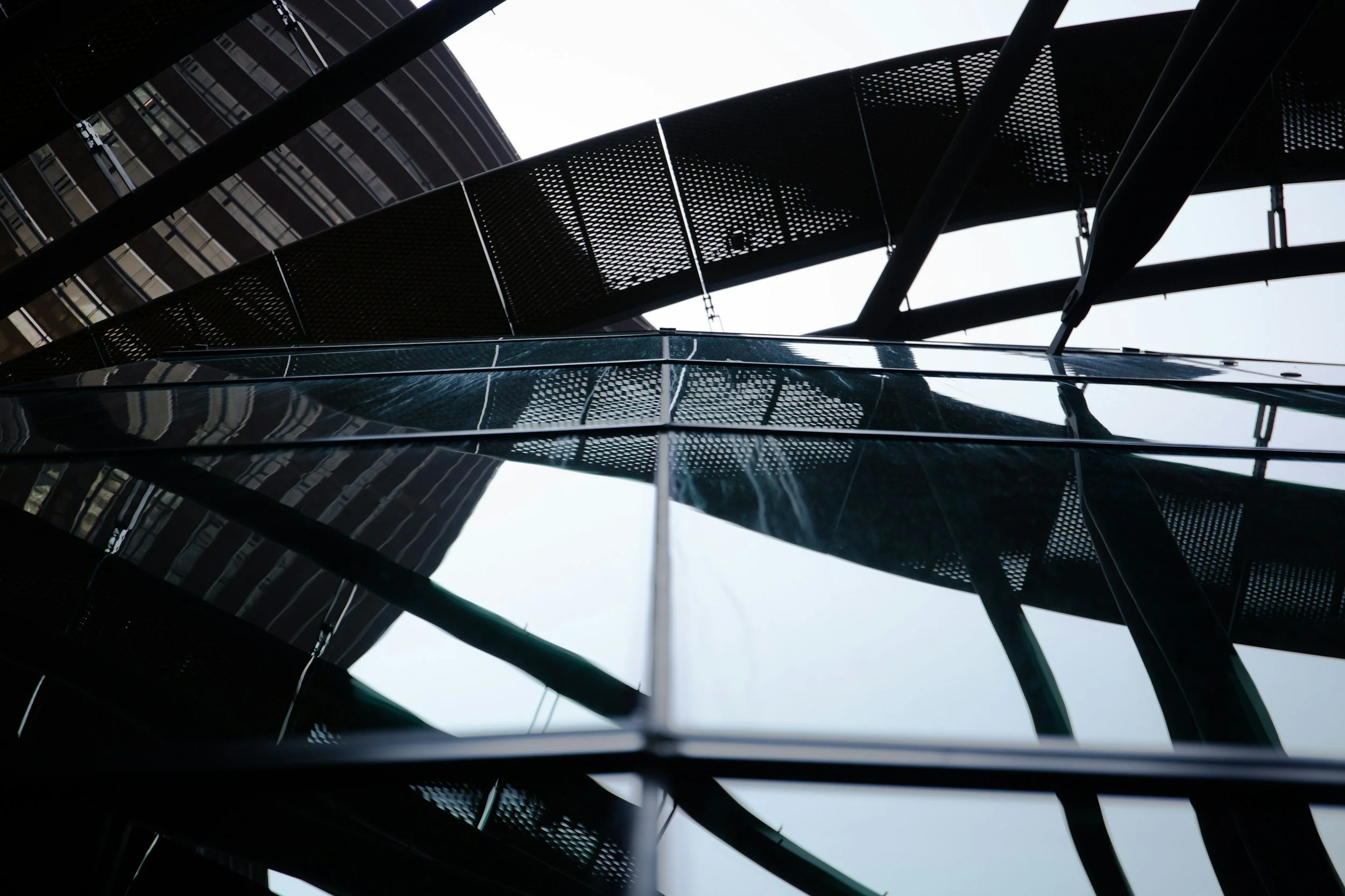 Looking upwards at a modern building's glass and steel exterior, with perspectives emphasizing the geometric lines and reflections.
