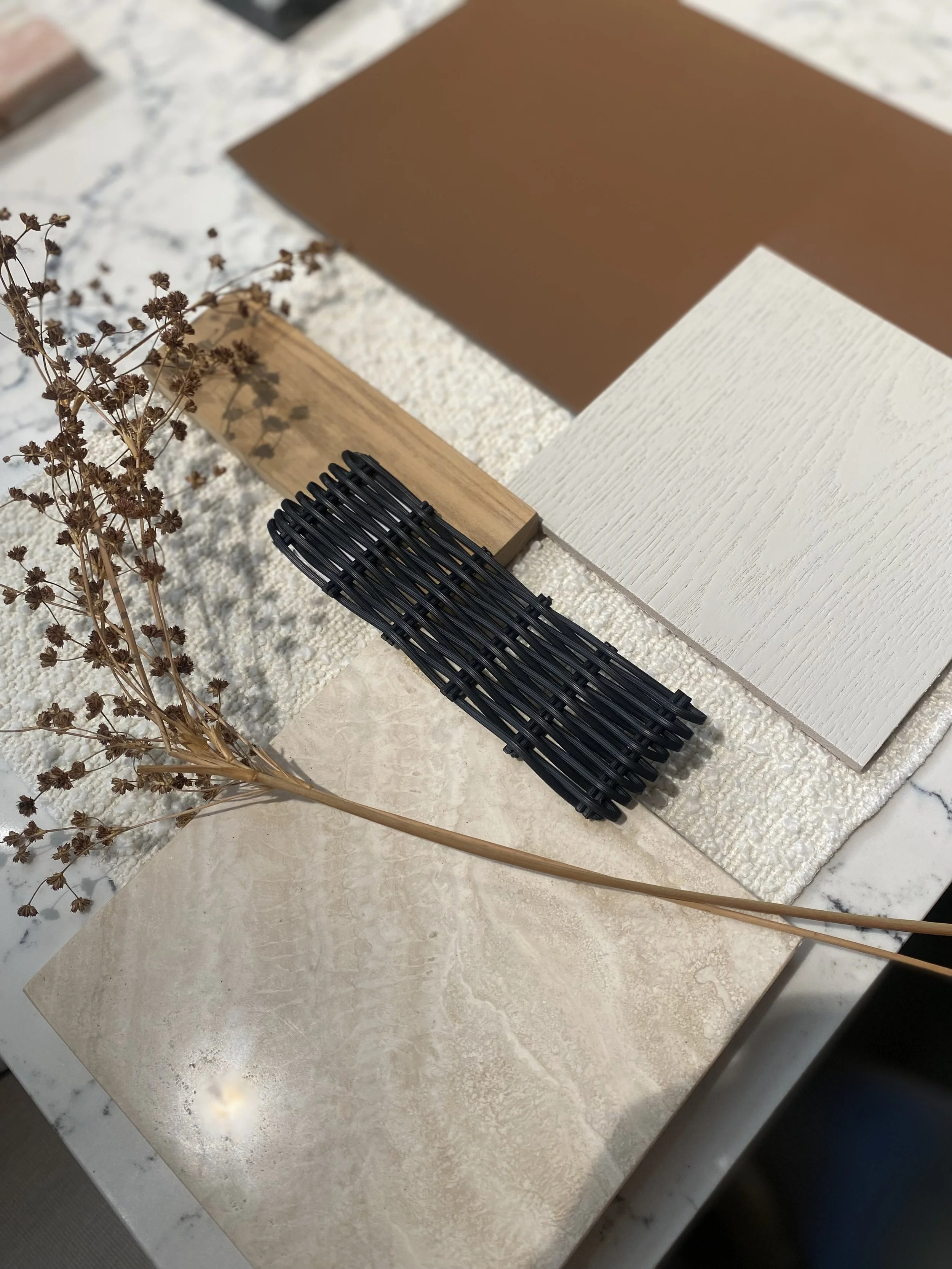 A tabletop display with various material samples including wood, fabric, and tile, accompanied by a dried branch and a black hair clip.
