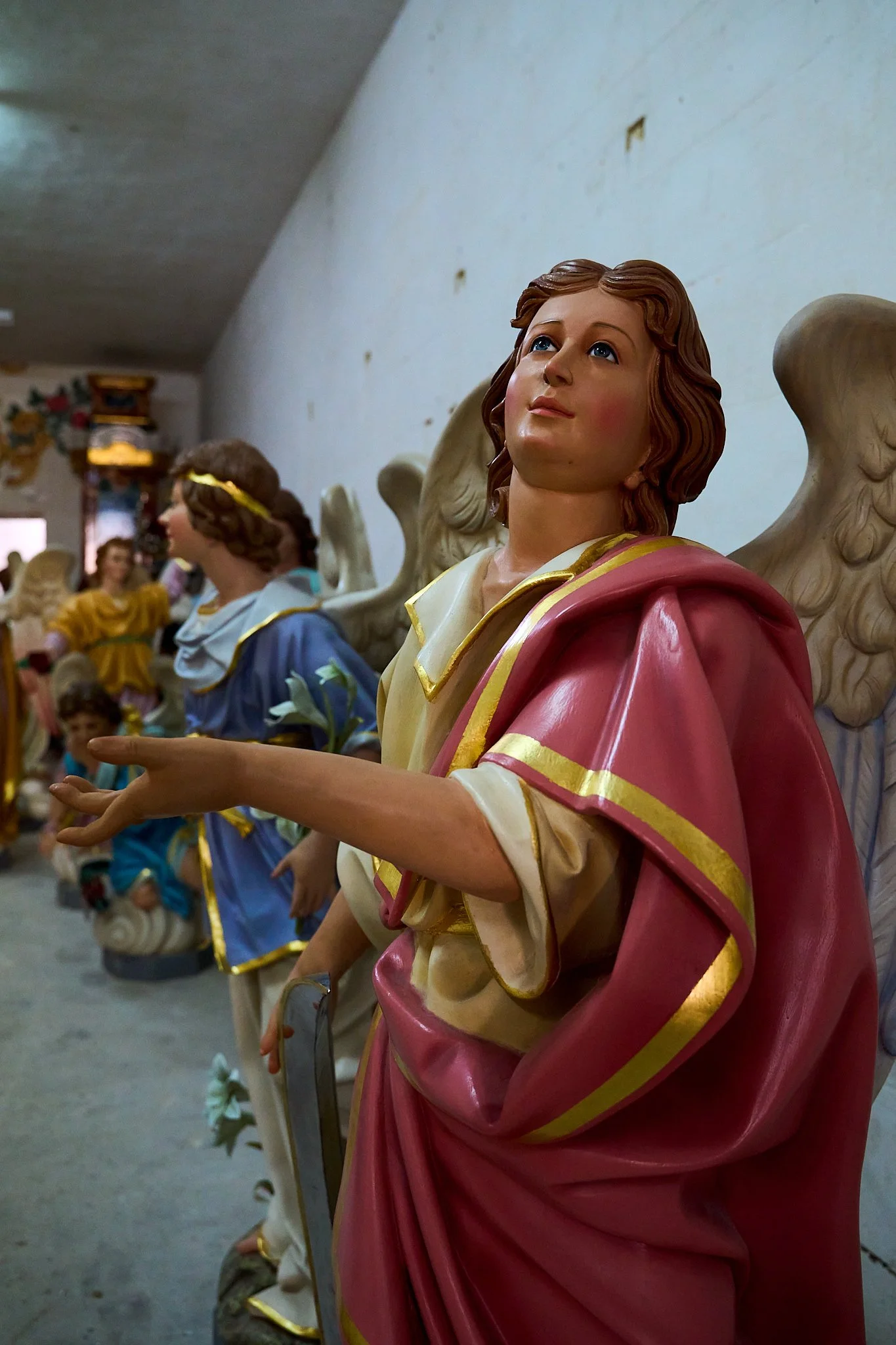 Near life-sized religious angels statues with intricate details, dressed in colorful robes, lined up inside a building.