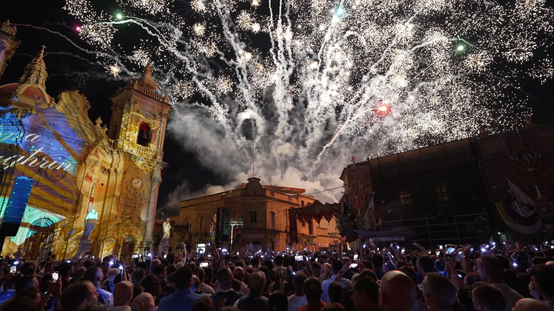 Crowd watching fireworks display in front of a historic church during nighttime celebration.