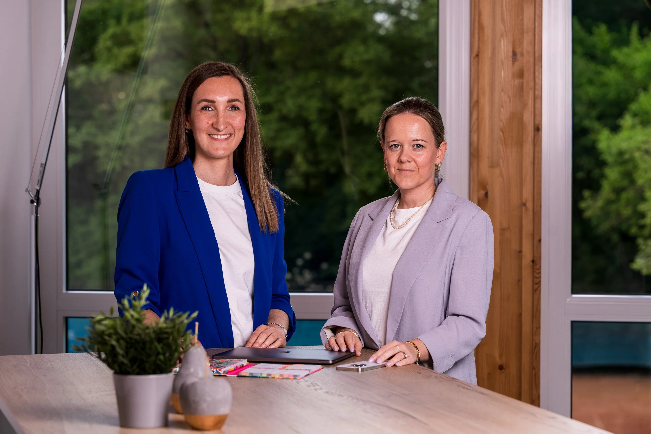 Zwei Frauen stehen an einem Tisch, vor Ihnen liegt Arbeitsmaterial für den Office-Alltag, beide sind schick gekleidet
